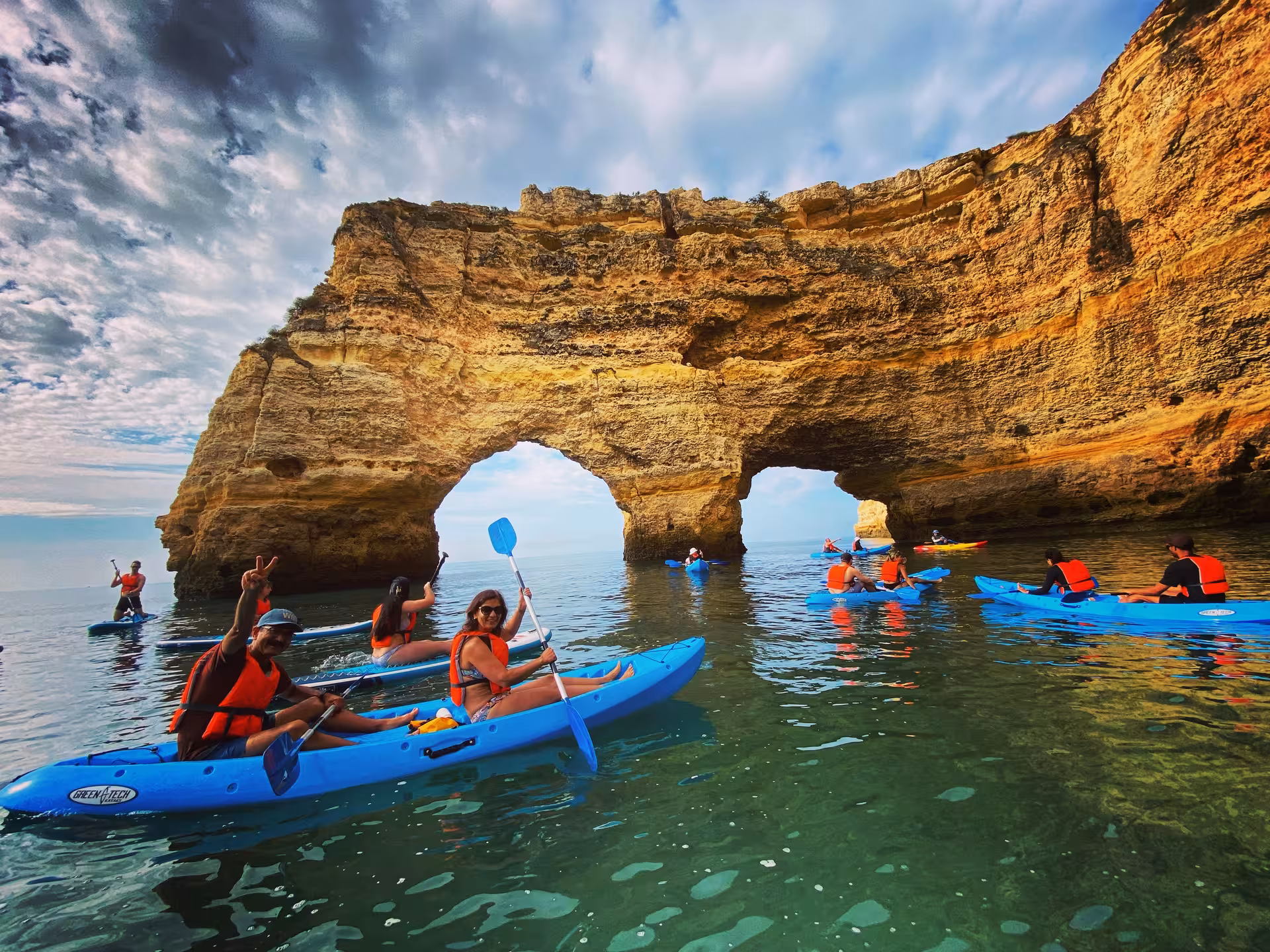 Group enjoying Benagil Caves kayak tour, paddling blue kayaks past Algarve sea arches and golden limestone cliffs in Portugal