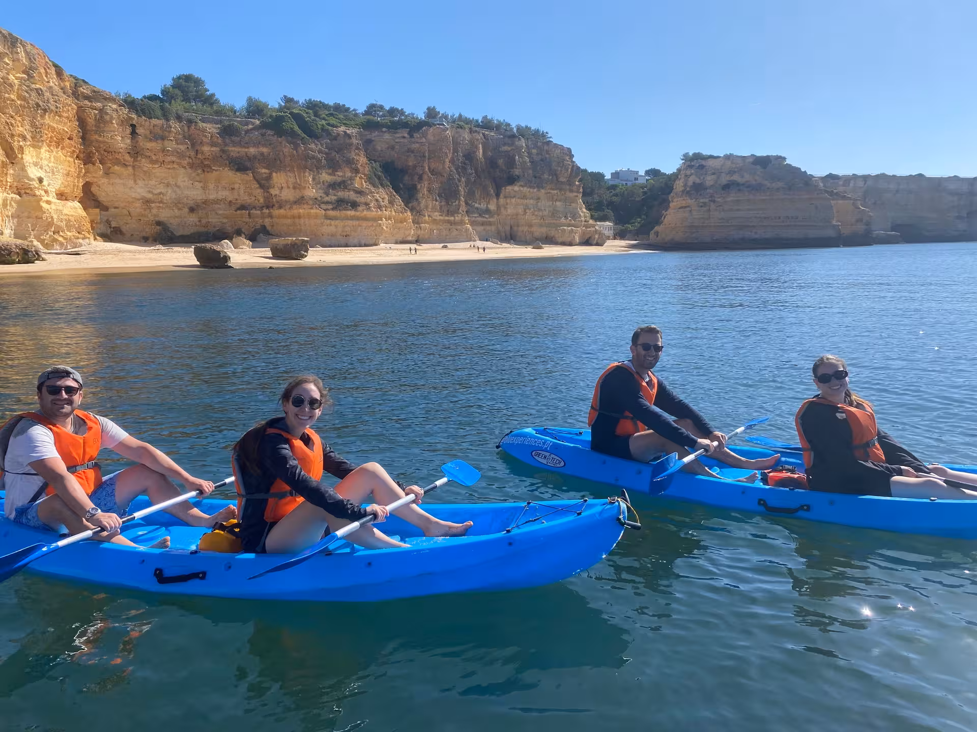 Small group in blue kayaks with life jackets paddling along Algarve cliffs on a Benagil Caves kayak tour in Portugal