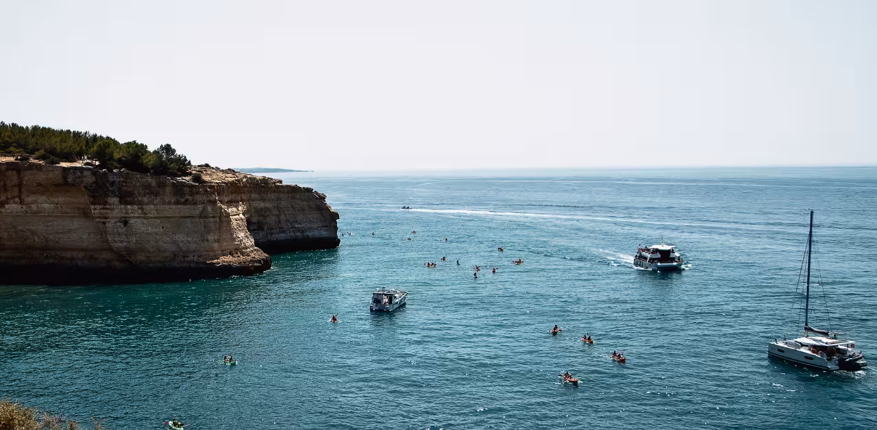 Kayakers and tour boats explore calm turquoise waters below Benagil cliffs on a guided Algarve coastal cave adventure