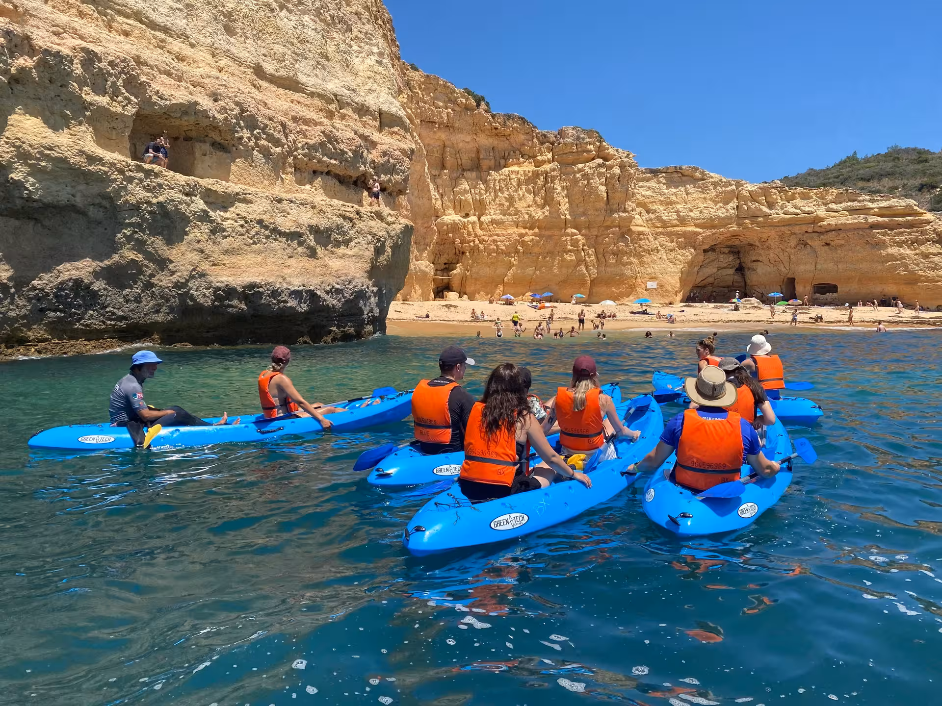 Group kayak tour approaching Benagil Beach in Algarve, paddling turquoise waters below dramatic golden limestone cliffs