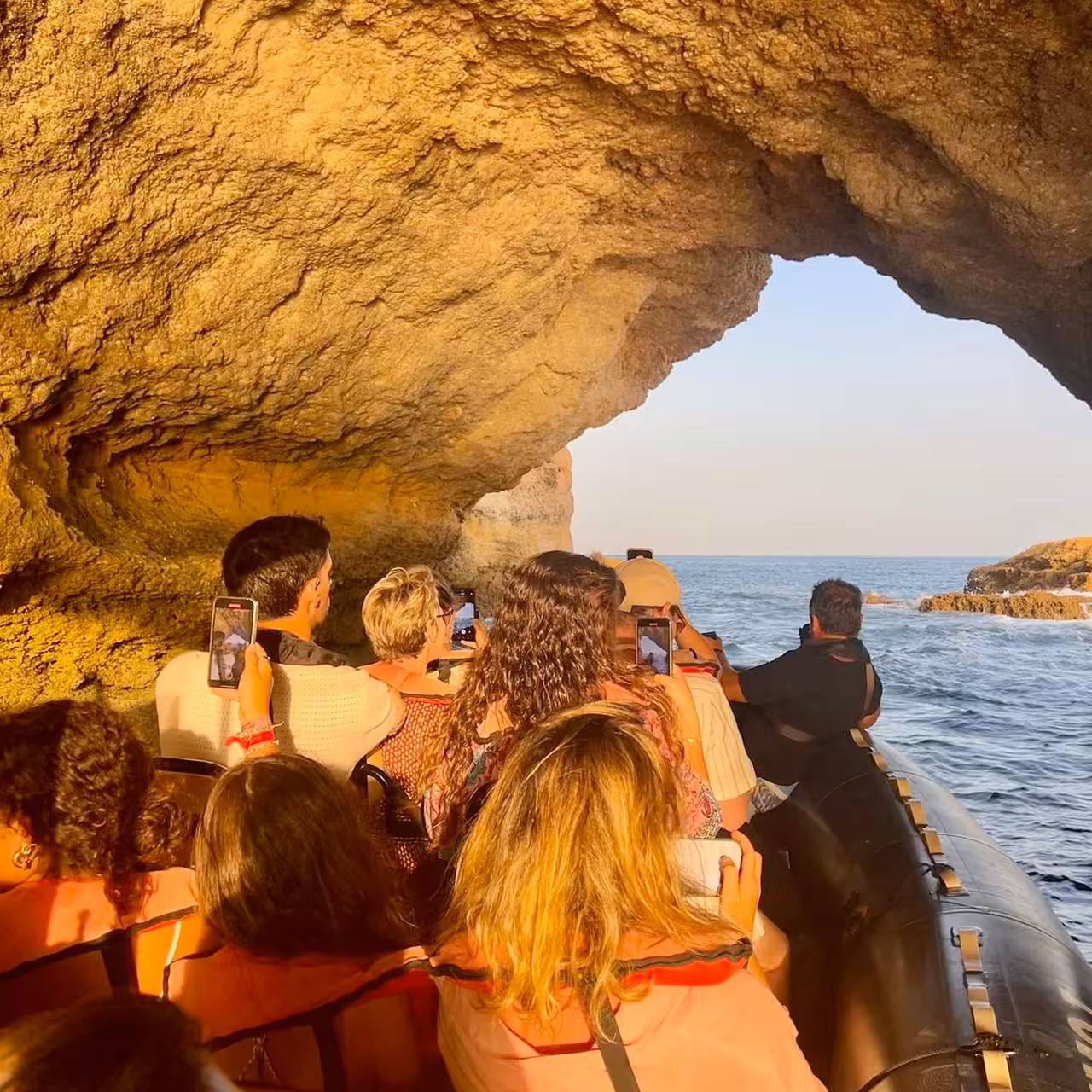 Travellers on a private Benagil Caves boat tour glide under a rocky arch, filming the Algarve coastline and Atlantic views