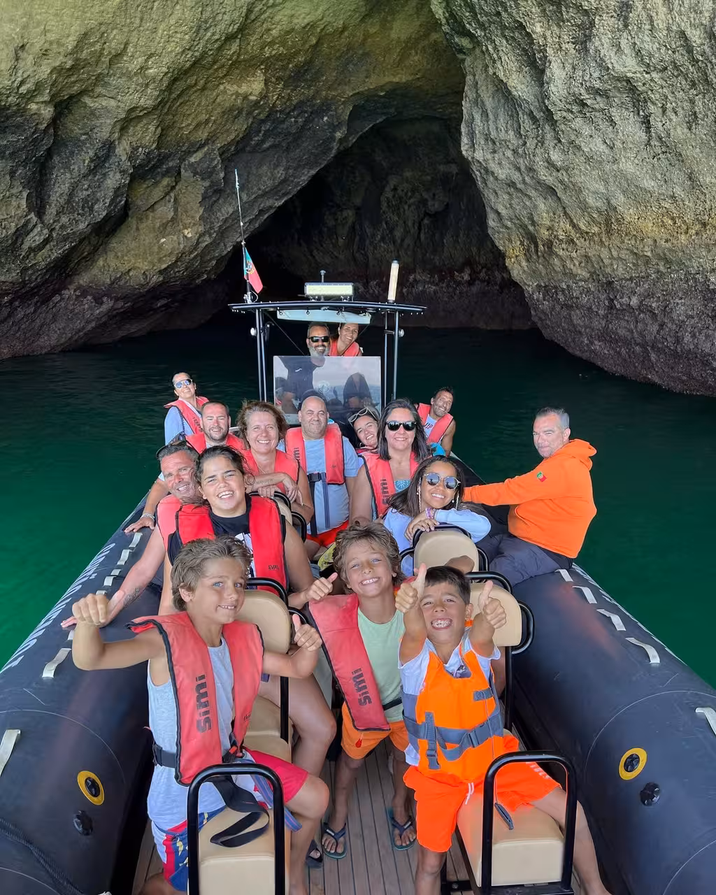 Happy group on RIB speedboat exploring Benagil Caves on private Algarve tour, smiling kids in life vests inside sea grotto