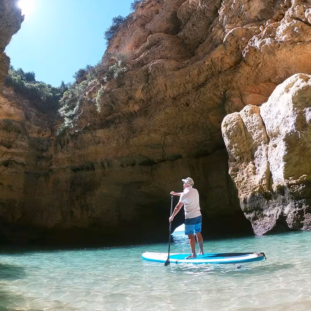 Solo paddler on SUP gliding through tranquil turquoise waters inside a dramatic Benagil cave on an Algarve sunset tour