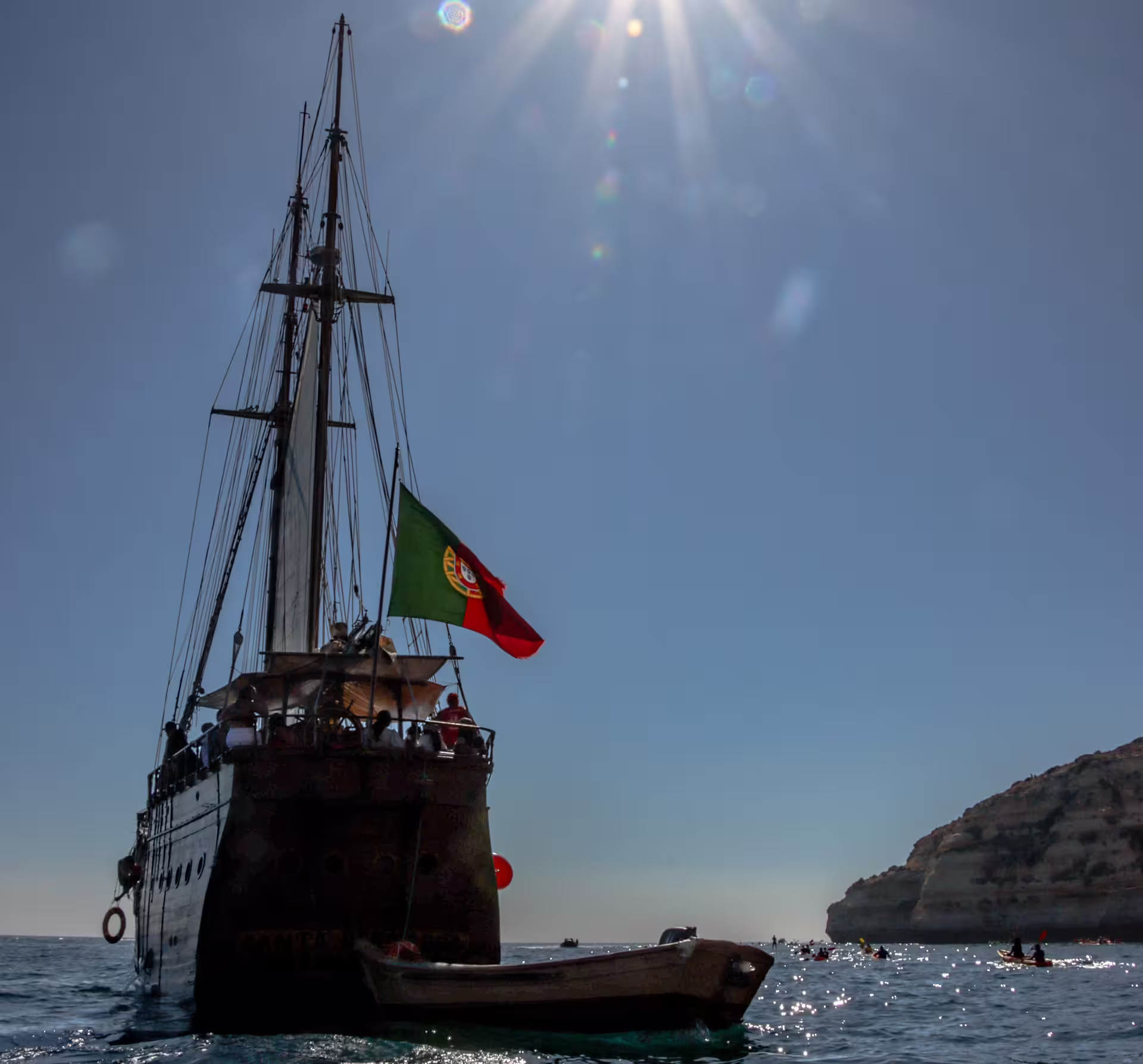 Majestic sailboat under bright sun near Algarve cliffs, showcasing Portugal's stunning coastal scenery.