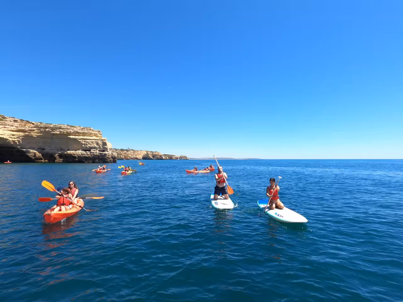 Group kayaking and paddleboarding near Benagil caves, enjoying the sunny Algarve coast adventure.
