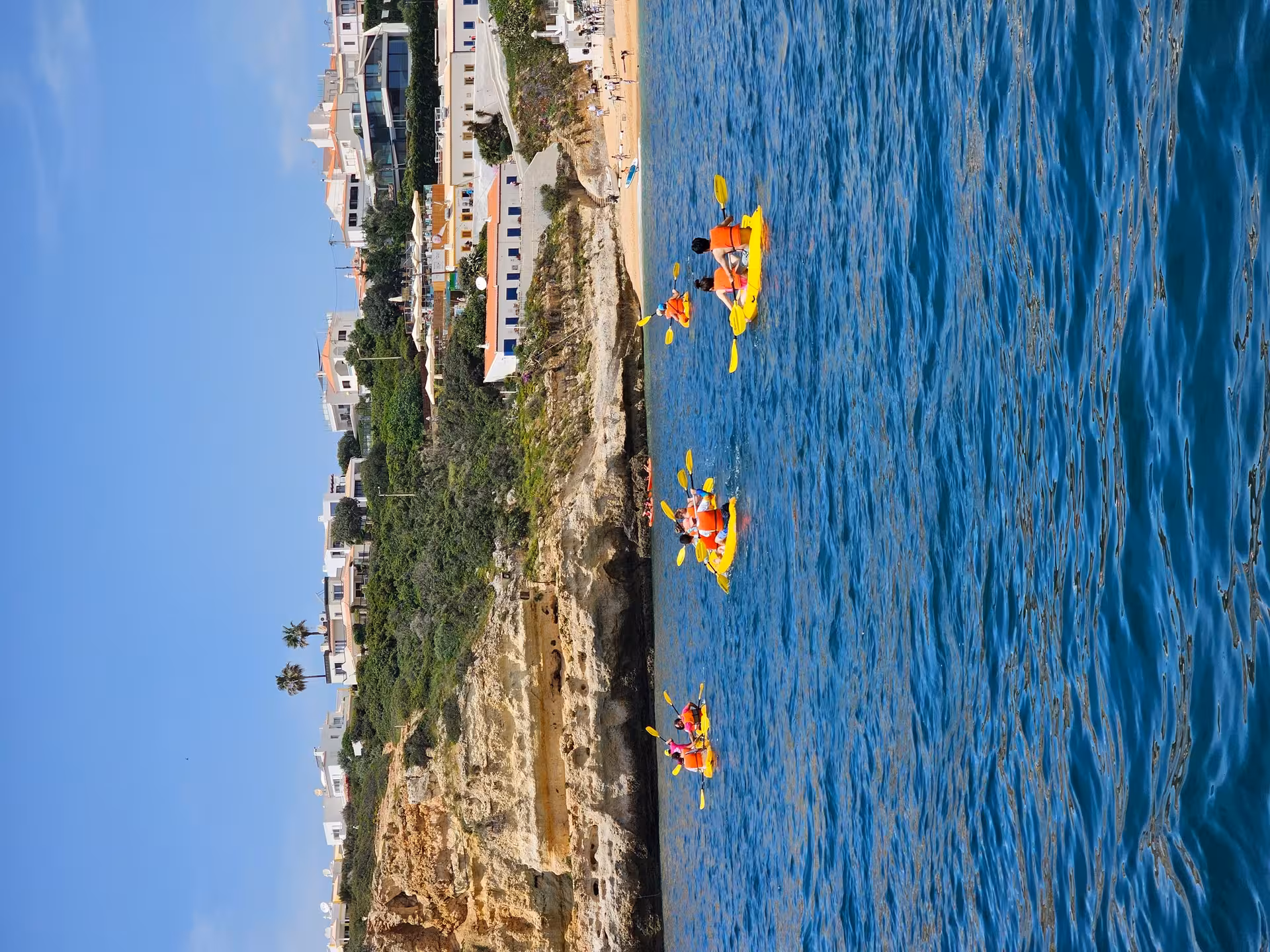 Kayakers in orange vests paddle yellow kayaks along Algarve cliffs from Benagil Beach, guided kayak rental experience