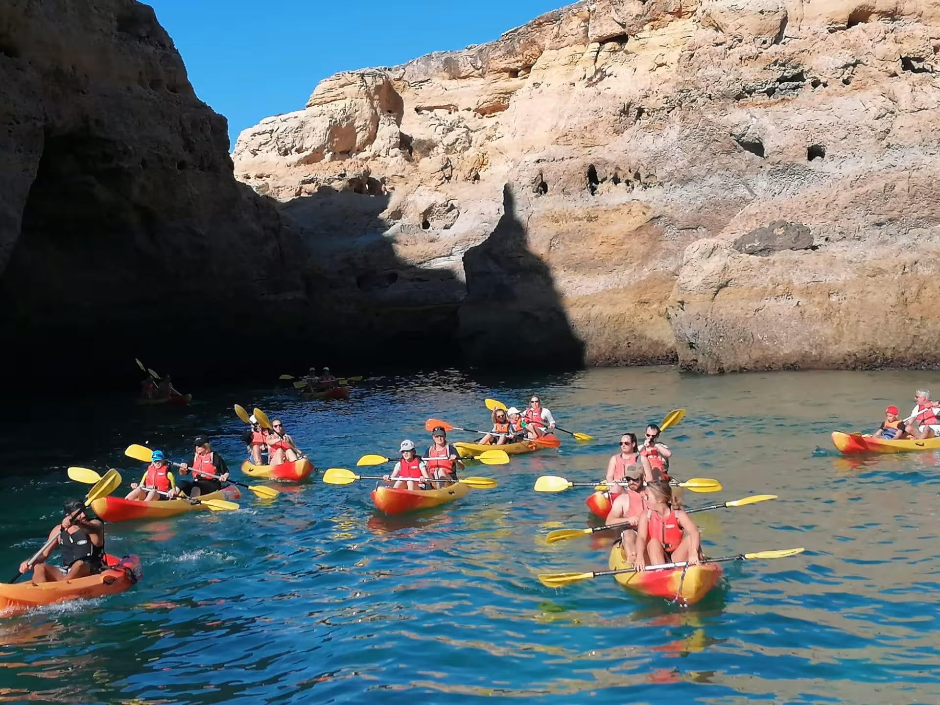Group of tourists paddling colorful kayaks along Benagil caves and golden cliffs on a guided Algarve coastal tour