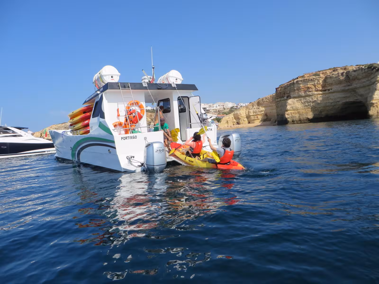 Guests launching colorful kayaks from support boat on Benagil kayak tour beside Algarve sea caves and sandy beach