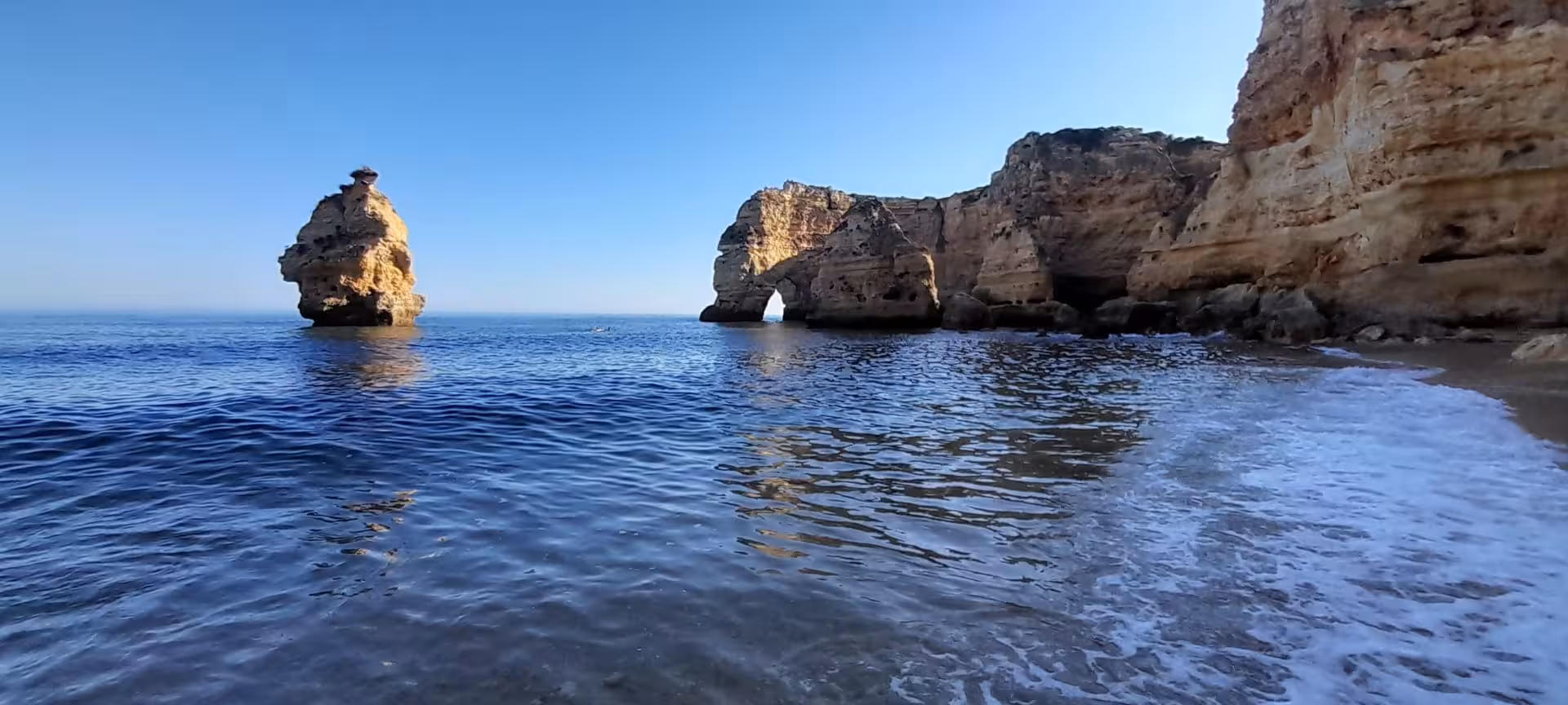 Rock arch and sea stack along rugged coastline, popular route for guided kayak tours with caves and ocean views