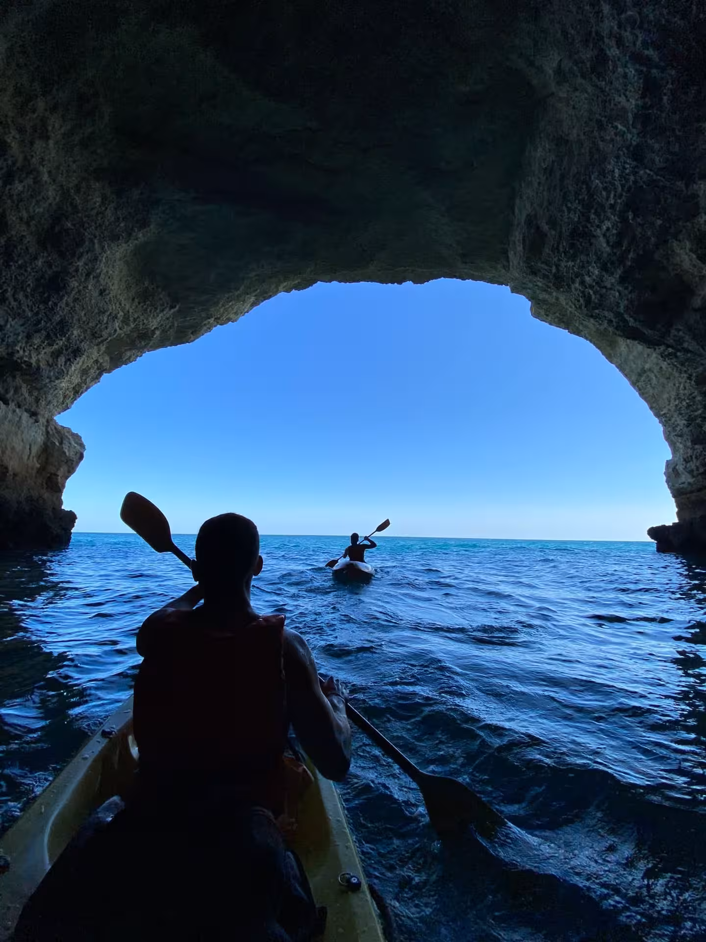 Kayakers paddling from a sea cave into open ocean, scenic coastal kayak tour with caves, cliffs and blue water