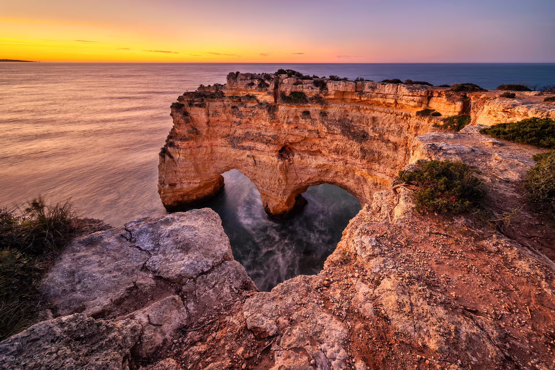 Dramatic sunset over Benagil sea arch with golden hues reflecting on the ocean, perfect for a kayak adventure.