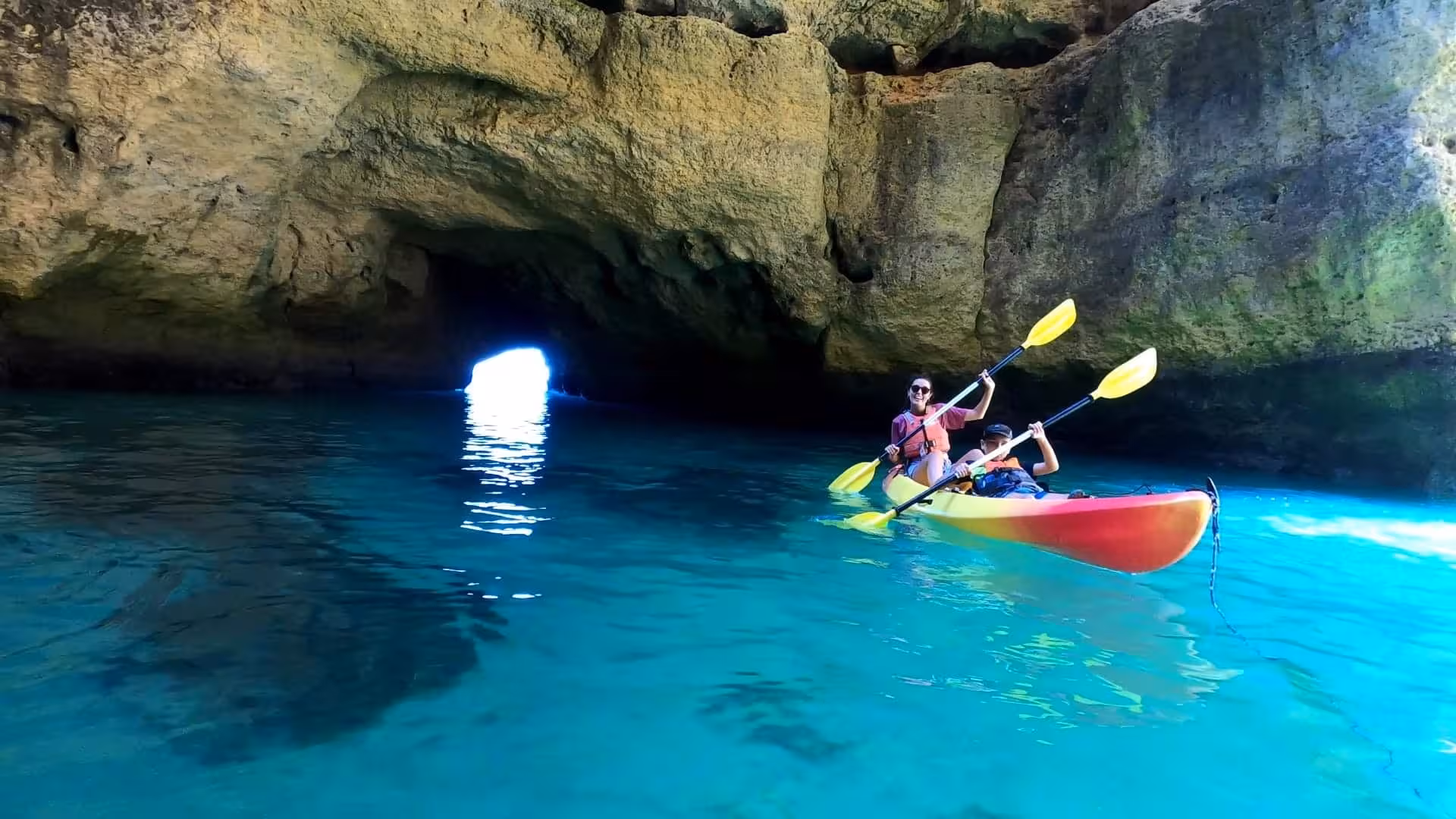 Family in a tandem kayak exploring the illuminated blue waters inside Benagil sea cave on a guided Algarve tour