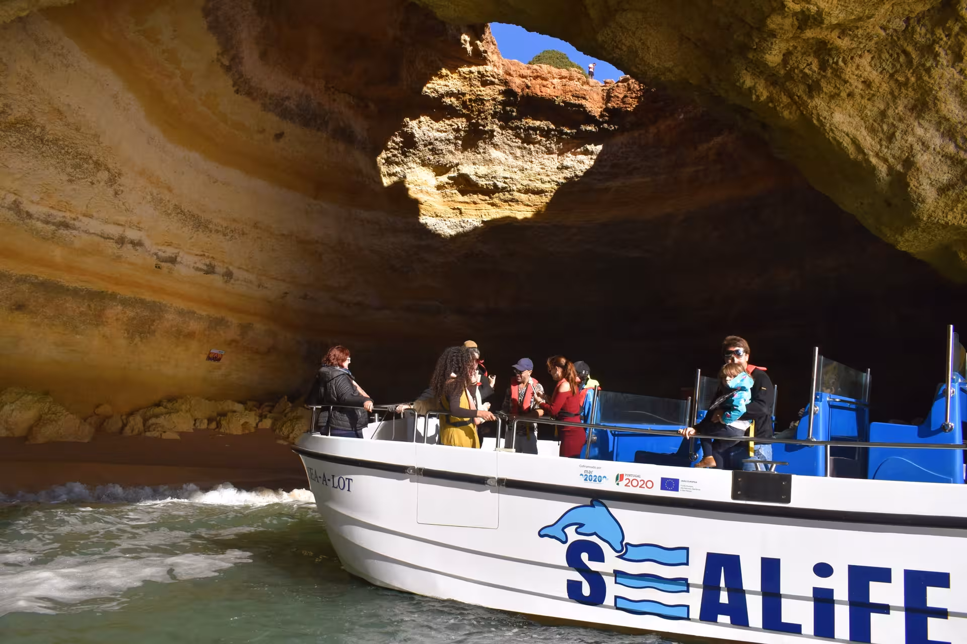 Tour boat entering the famous Benagil sea cave on an Algarve coastal cruise, with visitors admiring the golden rock formations