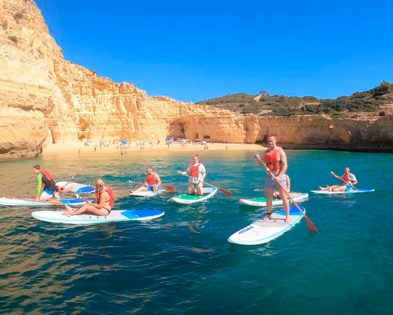 Paddleboarders enjoy a sunny day at Benagil Beach, exploring Algarve's stunning coastal cliffs and waters.
