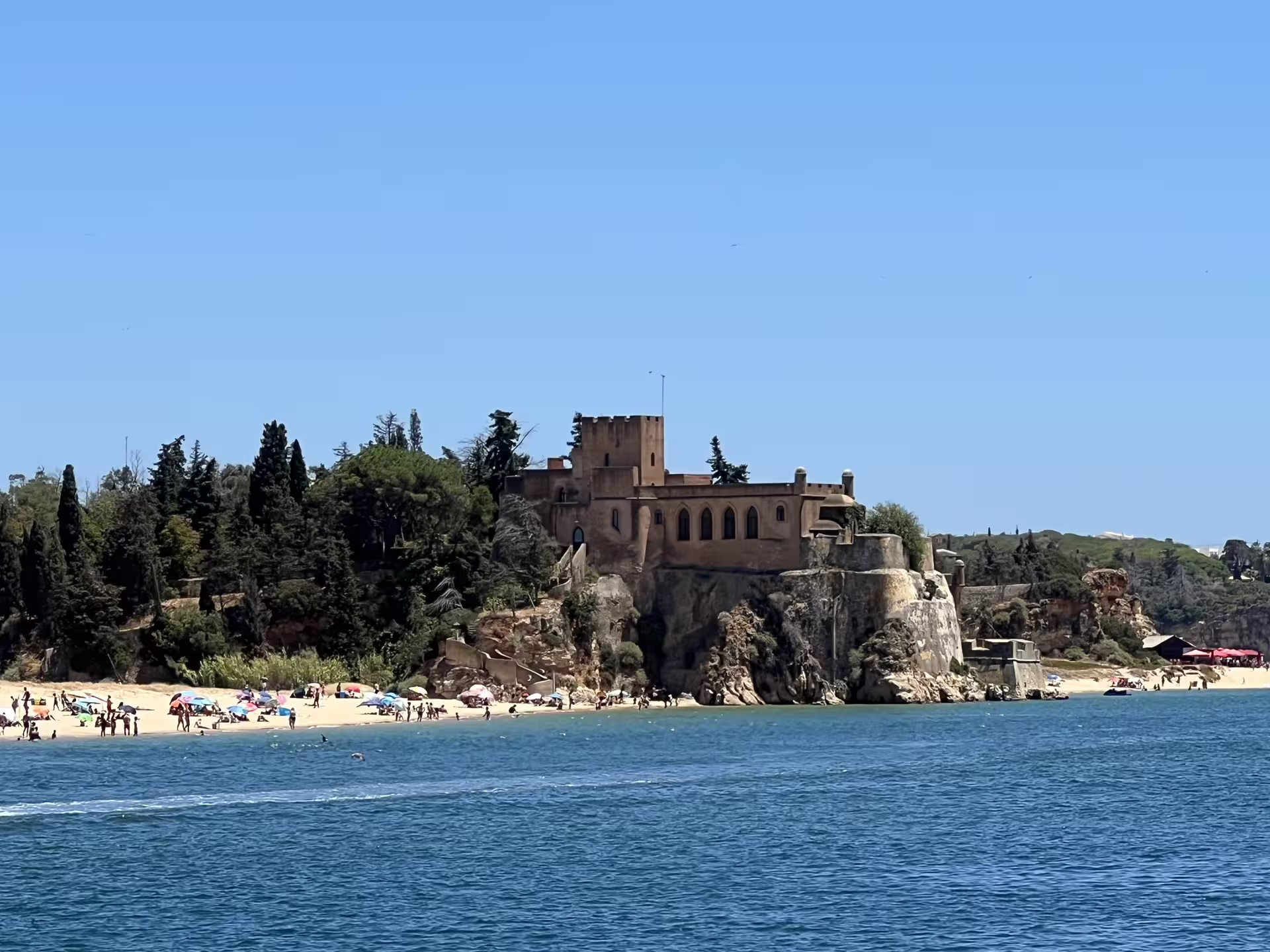 Scenic coastal view of a historic castle overlooking a sunlit beach and ocean near Benagil on a cruise tour.