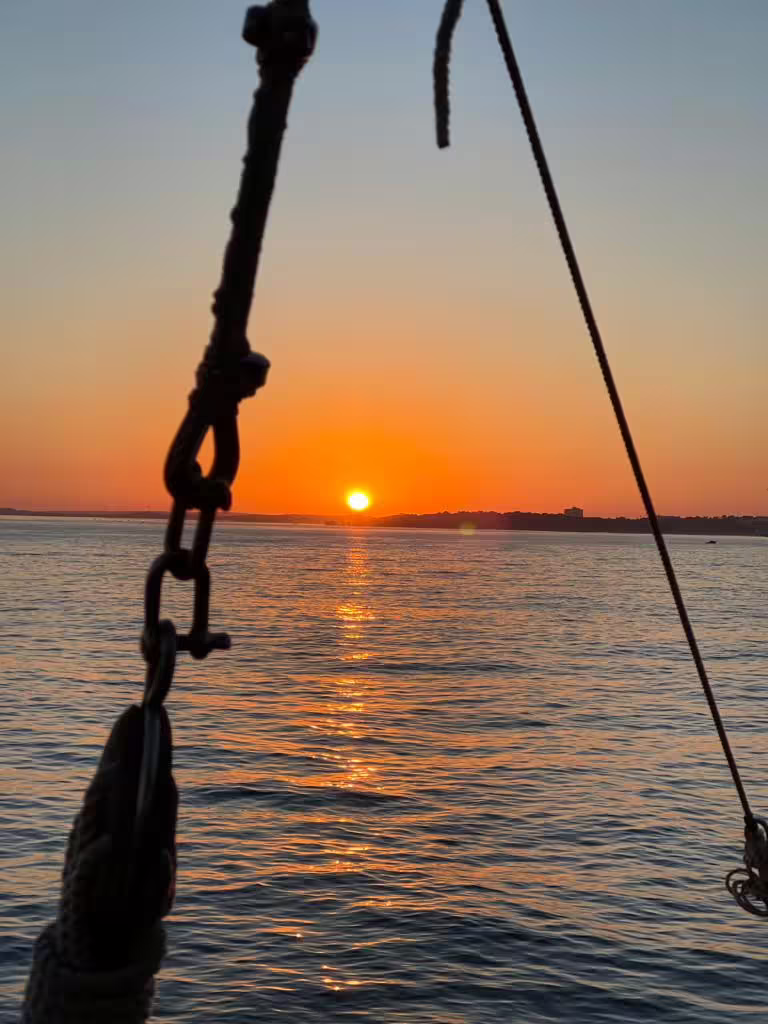 Silhouette of a ship's rigging against a vibrant sunset over calm waters, perfect for a romantic Benagil cruise.