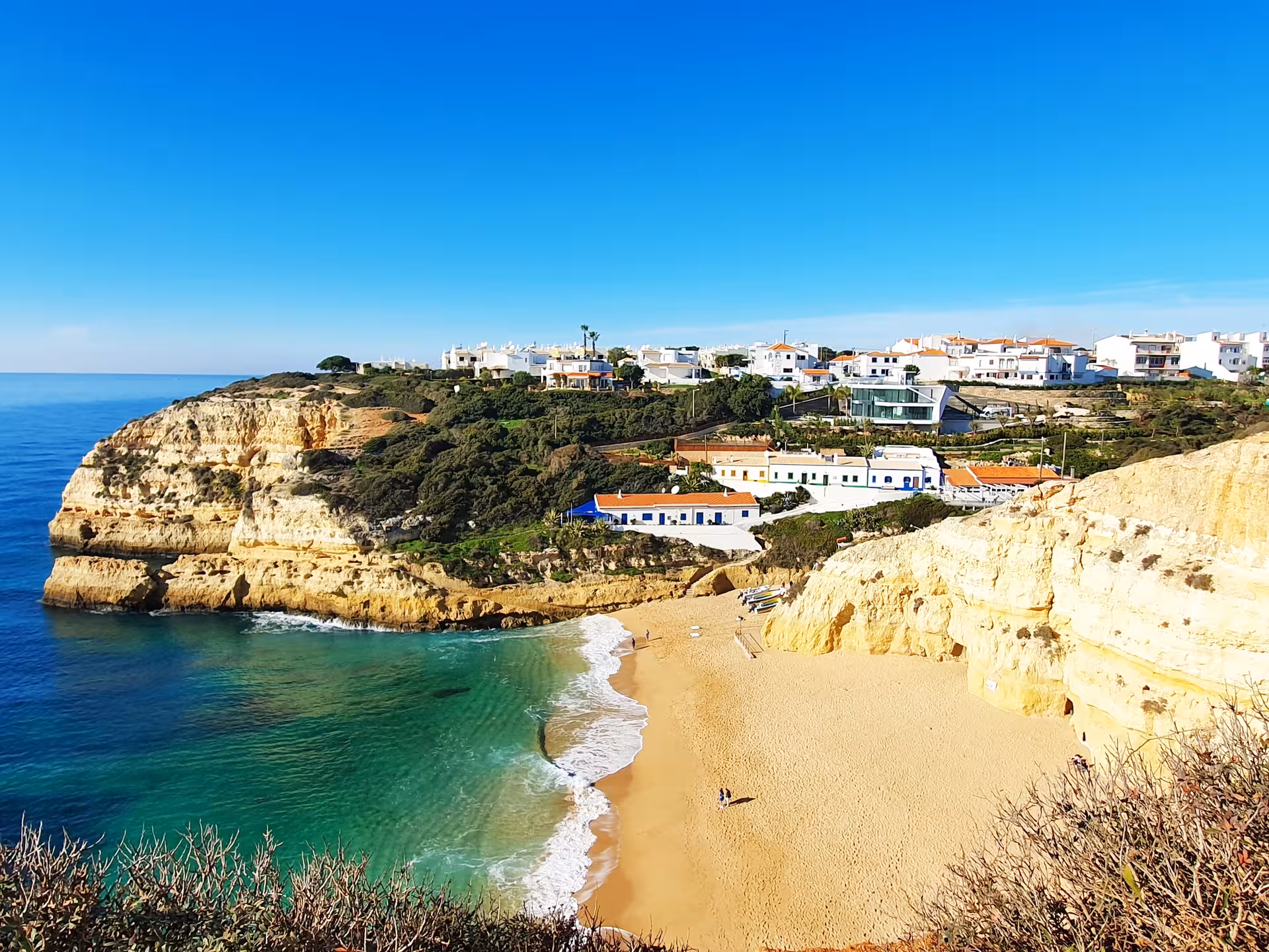 Scenic view of Benagil village above golden sandy beach, turquoise bay and limestone cliffs on Portugal’s sun-drenched Algarve coast