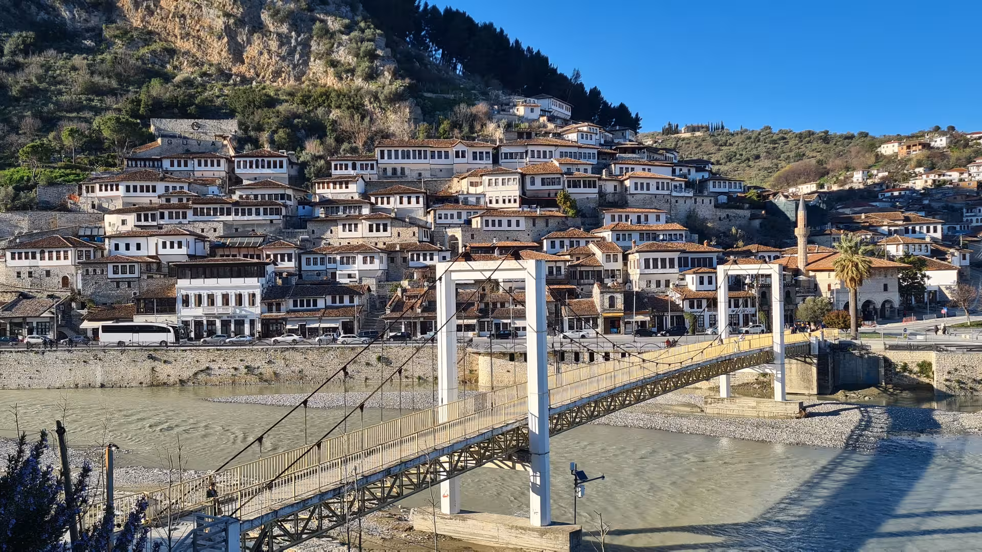 Panoramic view of Berat, Albania with iconic Ottoman architecture and a pedestrian bridge over the Osum River.