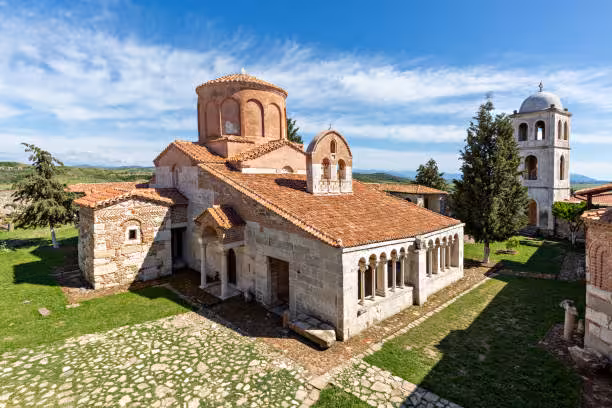 Historic Orthodox church with red-tiled roof and stone bell tower in Berat, Albania, under a clear blue sky.