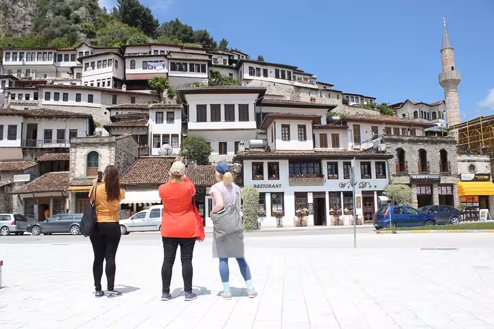 Tourists admire the historic Ottoman-era architecture in Berat during a guided walking tour under a clear blue sky.