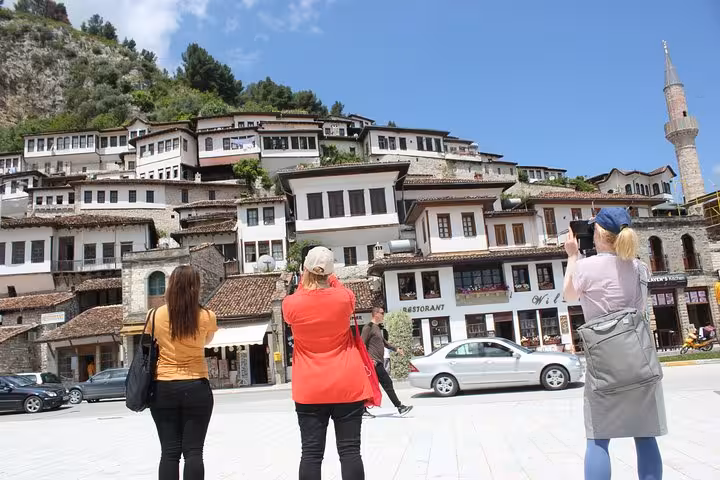 Travelers capture the stunning Ottoman architecture of Berat's hillside homes under a clear blue sky.