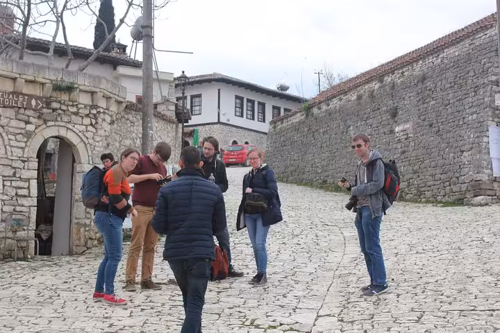 Group of tourists on a cobblestone street in Berat, Albania, guided tour of historic architecture and local culture.