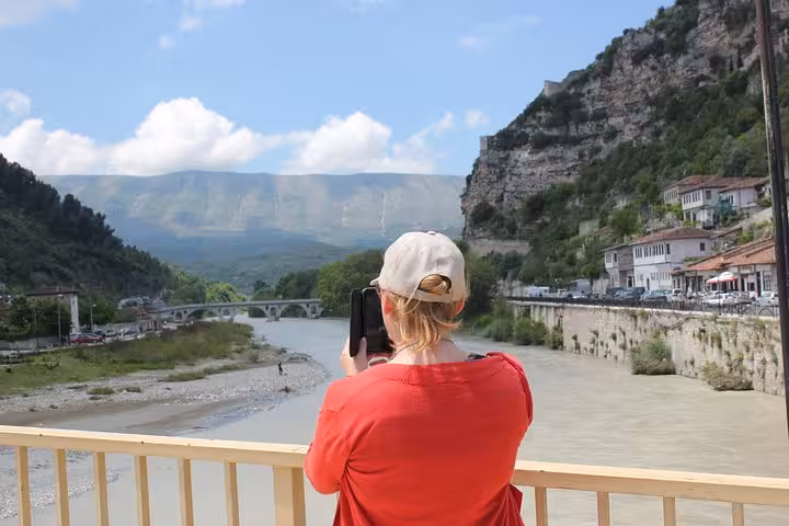 Tourist capturing scenic views of Berat's river and mountains, highlighting the beauty of this guided walking tour.