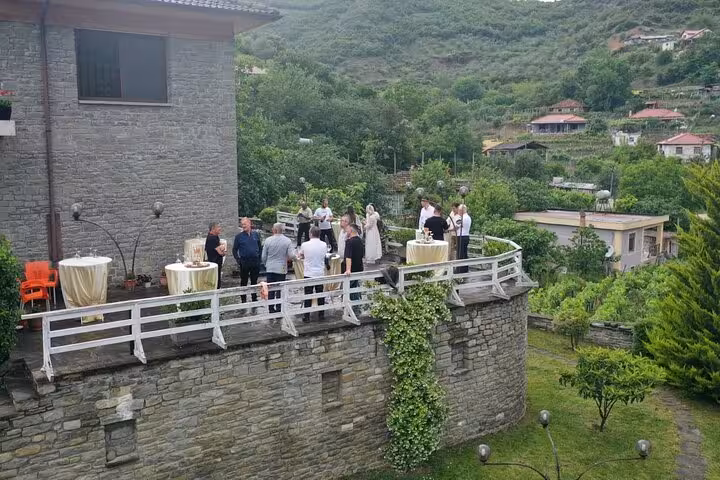 Group of people enjoying wine tasting on a terrace overlooking lush greenery in Berat's scenic countryside.