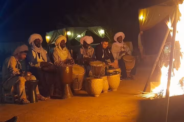 Traditional Berber musicians performing around a campfire under starlit skies in Merzouga Desert.