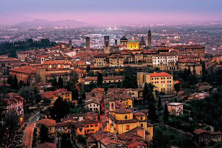 Twilight panorama of Bergamo Alta with glowing medieval towers and rooftops, seen on a 2.5-hour private walking tour