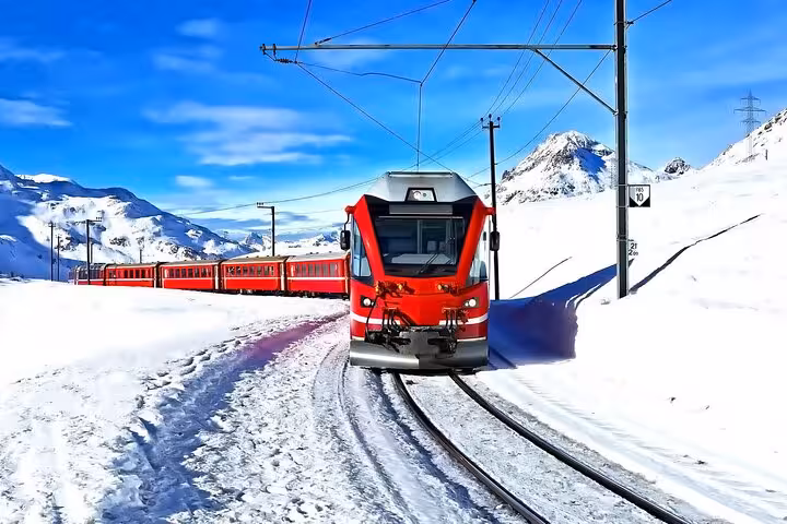 Red Bernina Express train crossing snow-covered Swiss Alps tracks on scenic ride to St. Moritz in winter