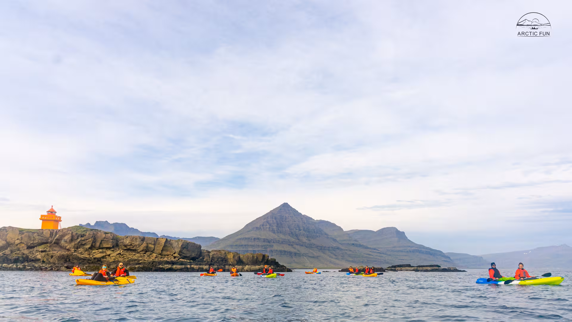 Group kayaking in Berufjörður with mountain backdrop, East Fjords Iceland, near orange lighthouse.