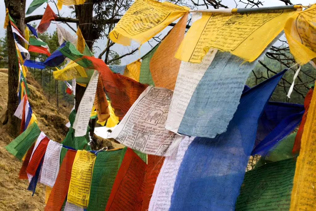 Colorful prayer flags fluttering in the wind against a backdrop of Bhutan's serene natural landscape.