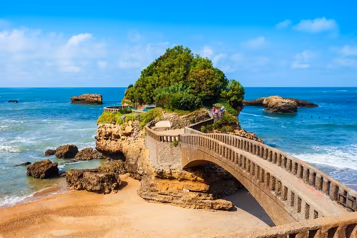 Picturesque stone bridge leading to a lush island on Biarritz's coastline, part of a guided city walk.