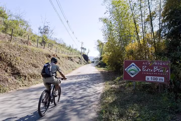 Cyclist exploring a countryside road with signage, highlighting Bike Rental by Paraty Tours experience.