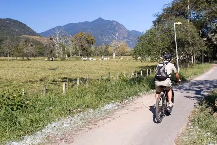Cyclist enjoying a scenic ride through lush fields and mountains with Bike Rental by Paraty Tours.