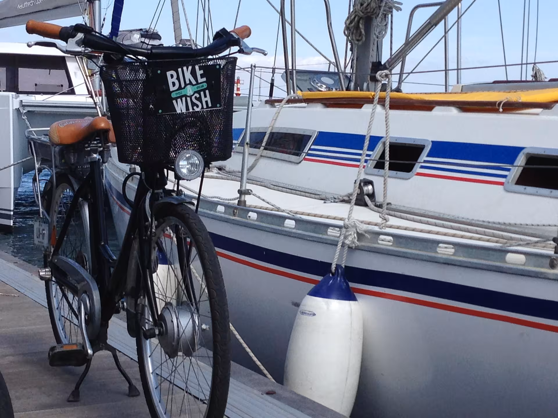 City bike parked beside a striped sailboat at the marina, meeting point for bike tour with boat sailing adventure