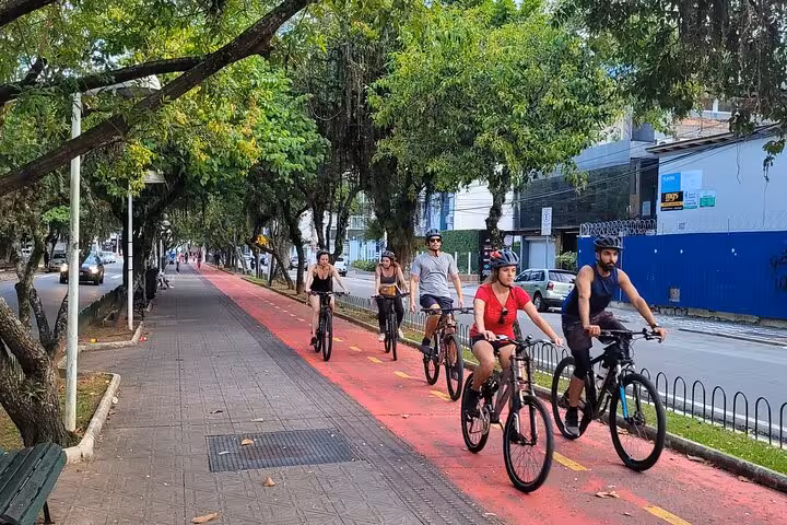 Cyclists enjoying a scenic bike path tour in Florianopolis, surrounded by lush greenery and vibrant street life.