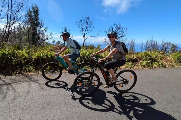 Cyclists enjoy a scenic bike tour on Madeira's west coast, riding along lush landscapes with ocean views under a clear blue sky.