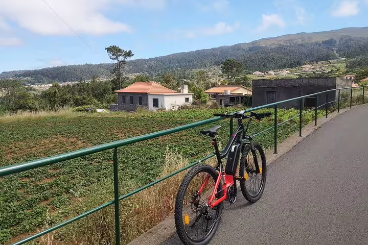 Scenic bike tour on Madeira's west coast with stunning views of lush landscapes, rural houses, and mountain backdrops.