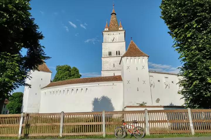 Fortified white church with clock tower in Transylvania, with a red mountain bike leaning against a wooden fence