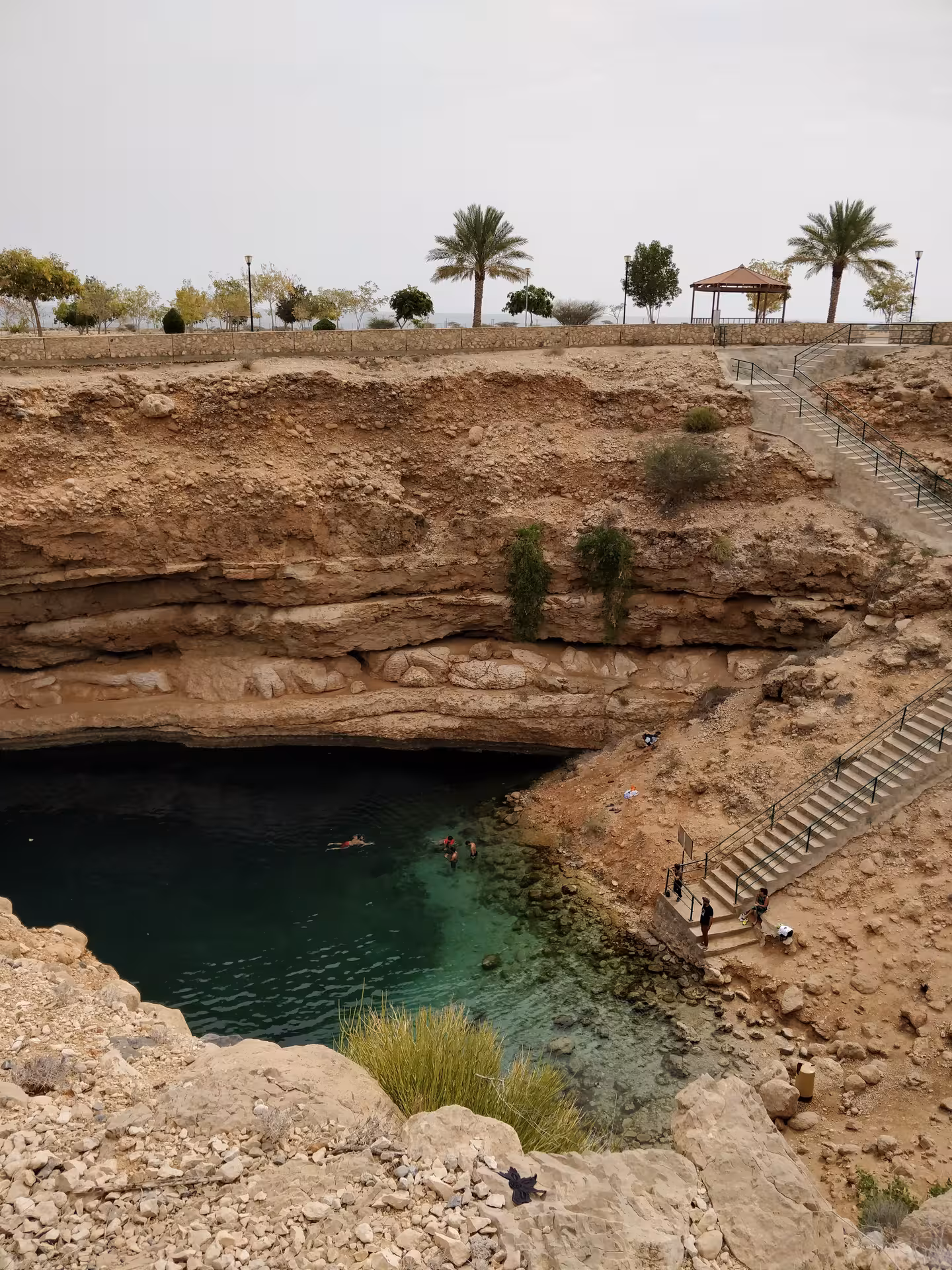 Visitors swim in the emerald waters of Bimmah Sinkhole, reached by stone steps on a Wadi Shab full-day tour in Oman