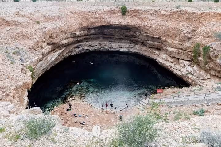 Aerial view of Bimmah Sinkhole’s turquoise pool and rocky crater with visitors exploring on a guided Wadi Shab day tour