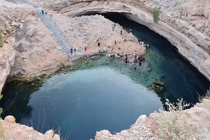 Tourists enjoy the stunning turquoise waters of Bimmah Sinkhole during a full-day tour from Muscat.