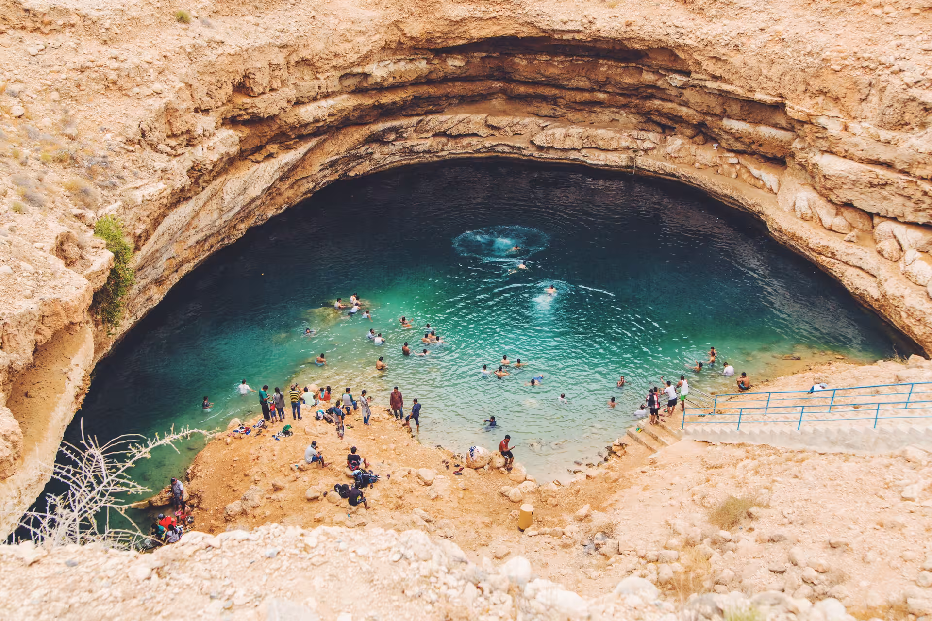 Visitors swim in the turquoise waters of Bimmah Sinkhole, a must-see stop on the Wadi Shab full day tour in Oman