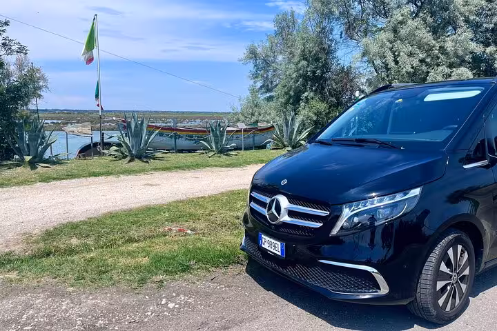 Luxurious black Mercedes van by serene lakeside en route from Milan MXP airport to Milan city center.