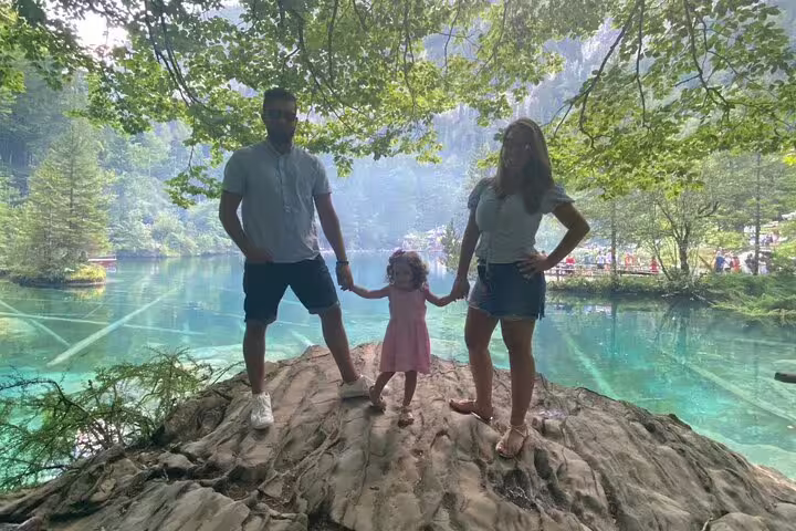 Family enjoying a picturesque view at Blausee Lake, with vibrant turquoise water and lush forest backdrop.
