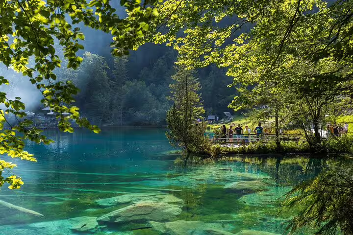 Tourists admire the crystal-clear waters and lush greenery of Blausee Lake on the Interlaken Private Tour.