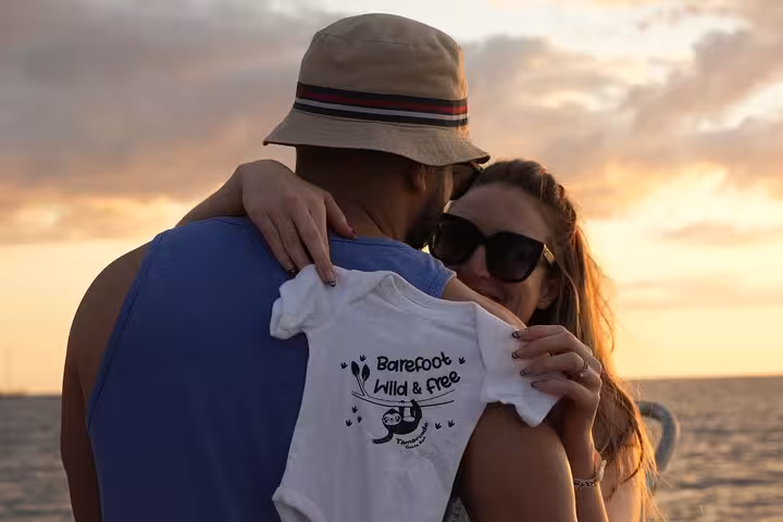 Couple holds a playful baby shirt on the Blue Dolphin Catamaran Tour during a romantic sunset cruise.