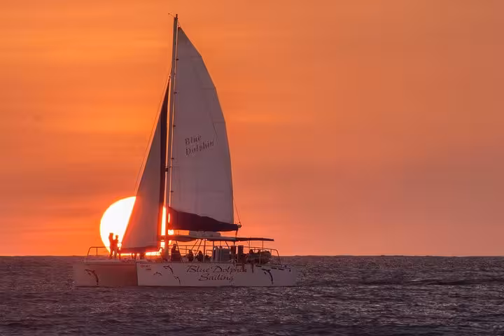 Catamaran sailing into a stunning sunset on the Blue Dolphin public tour, offering picturesque ocean views.